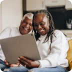 A senior couple sit on a sofa and use a tablet together.  